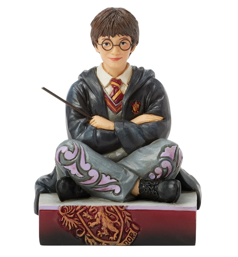 Figurine of Harry Potter in a gray robe with a wand, sitting on a red and gold box.