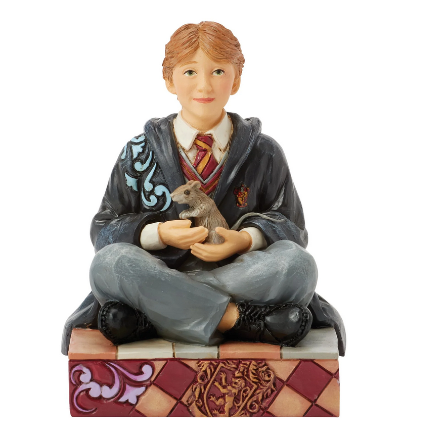 Front of figurine of Ron Weasley in a robe holding a rat, sitting on a box with Gryffindor emblem.