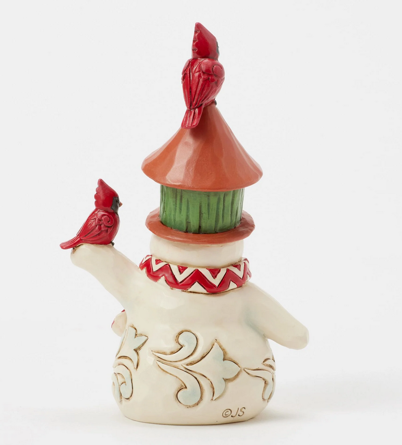 Back of snowman figurine with a birdhouse on its head and two red birds, against a white background