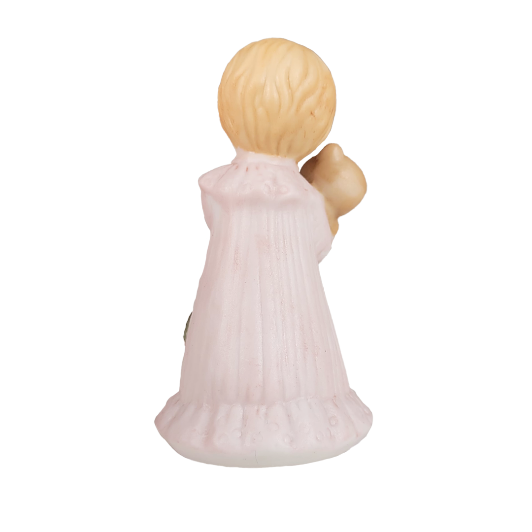 Back of figurine of a child in a pink dress holding a teddy bear on a white background