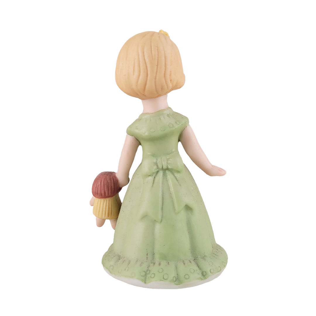 back of girl figurine in green dress holding doll on white background