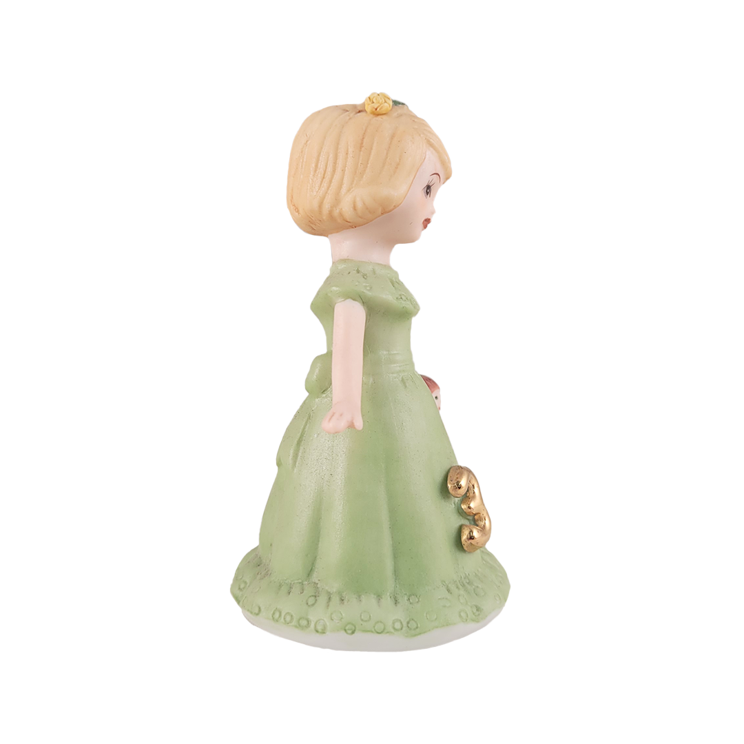 side of girl figurine in green dress holding doll on white background