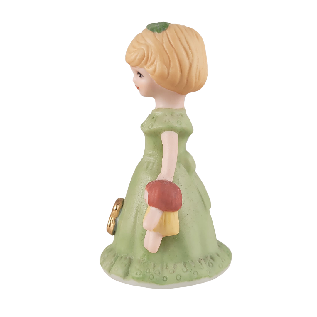 side of girl figurine in green dress holding doll on white background