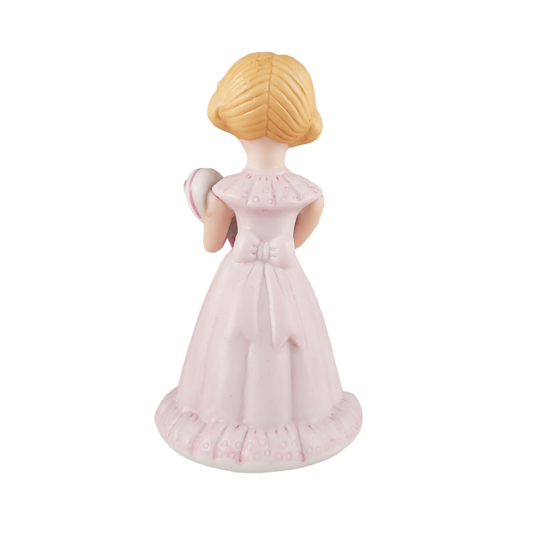 Back of figurine of a girl in a pink dress with a gold emblem on a white background