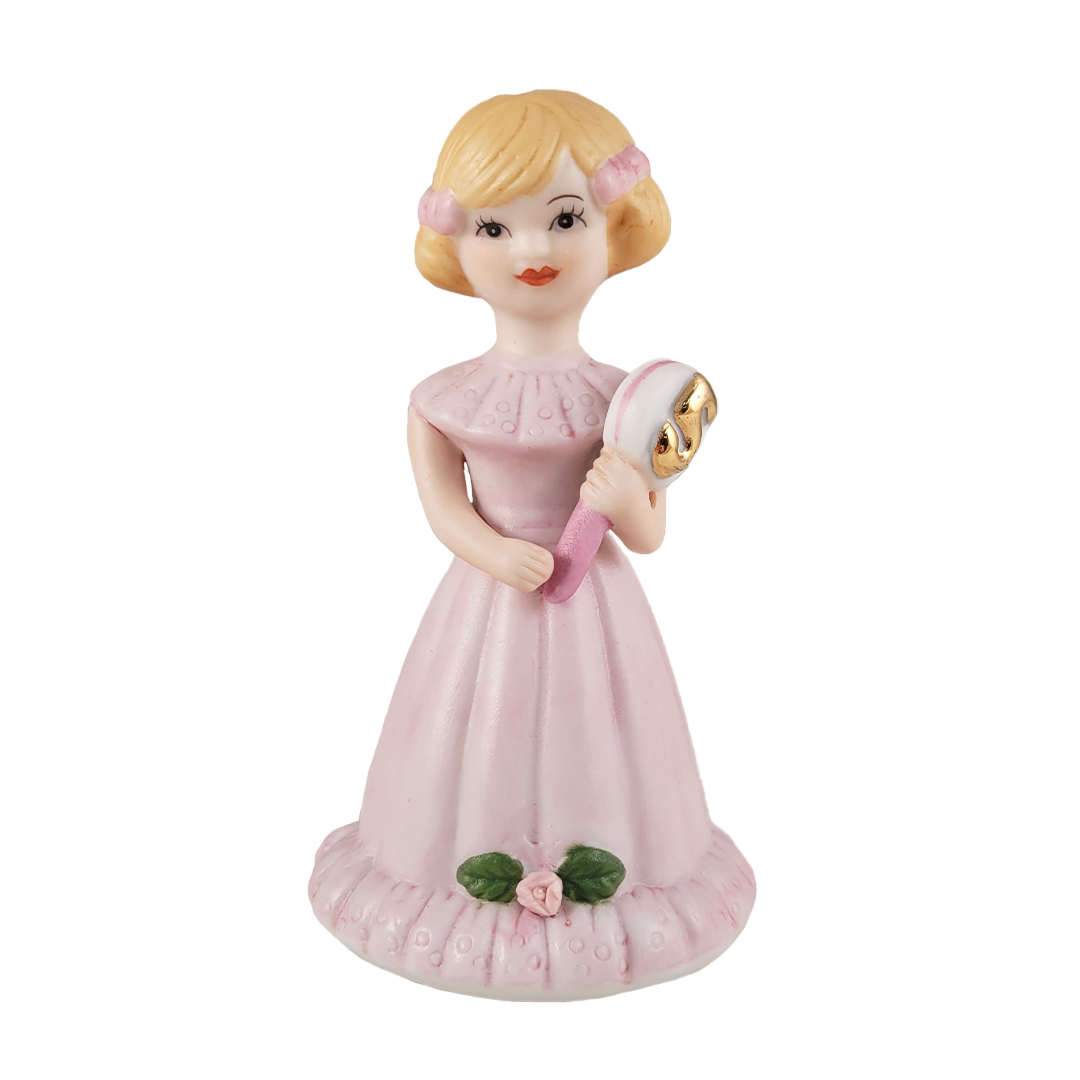 front of figurine of a girl in a pink dress with a gold emblem on a white background