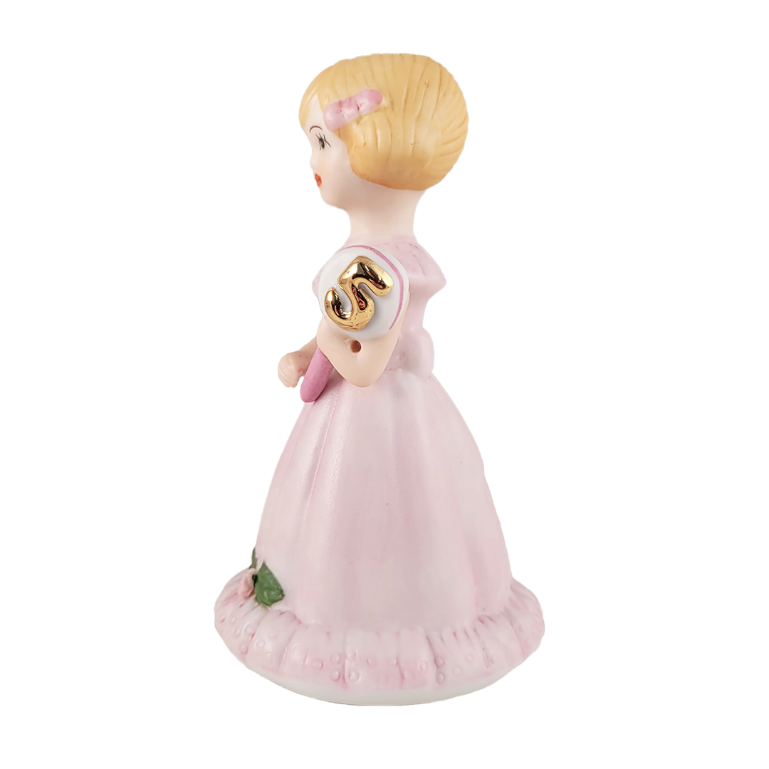 Side of figurine of a girl in a pink dress with a gold emblem on a white background