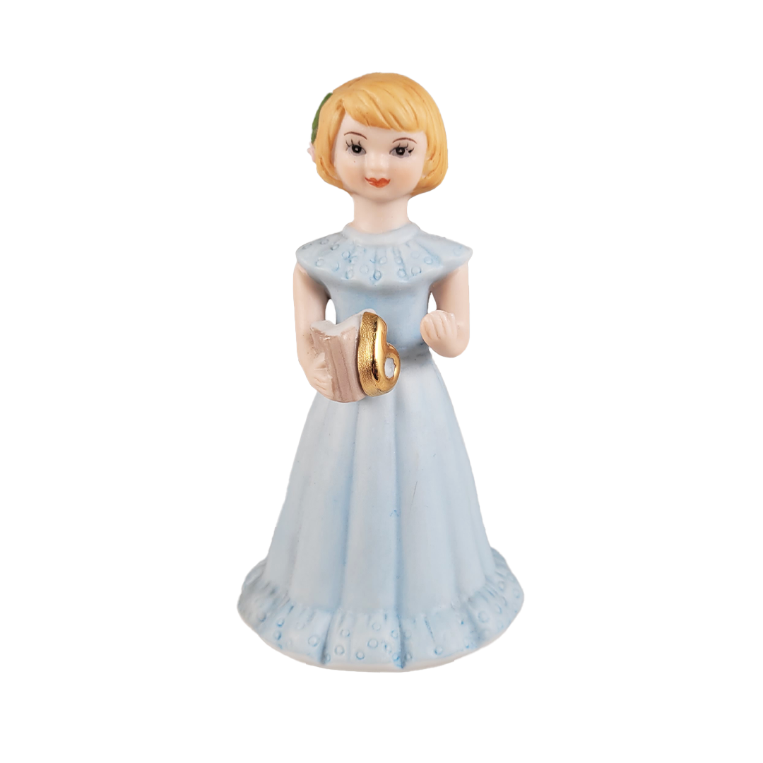 Front of figurine of a girl in a light blue dress holding a book on a background