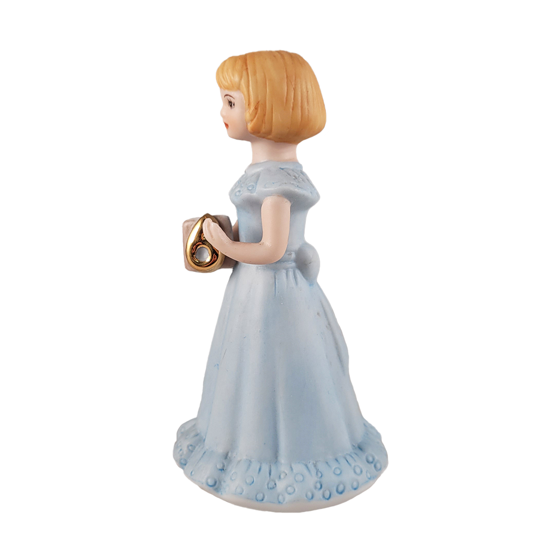 Side of figurine of a girl in a light blue dress holding a book on a background
