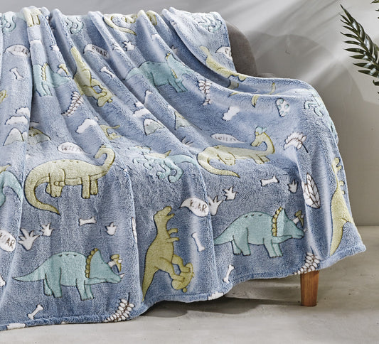A blanket with glow-in-the-dark dinosaur patterns spread over a couch, depicting various dinosaurs and glowing in a dimly lit room.
