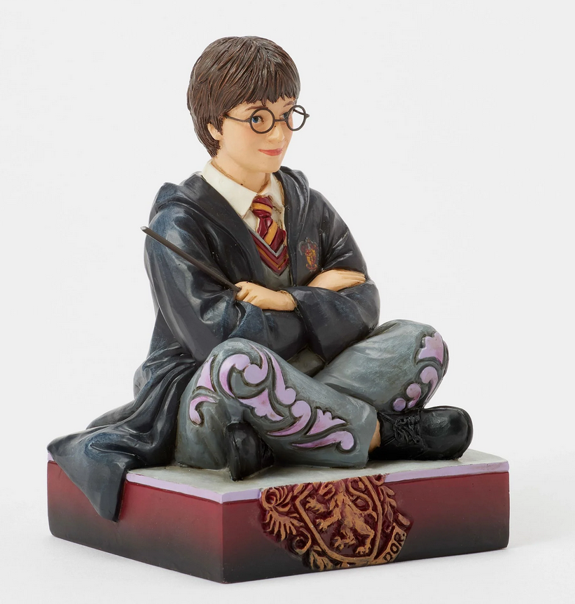 Figurine of Harry Potter in a robe, sitting on a box with Gryffindor emblem.