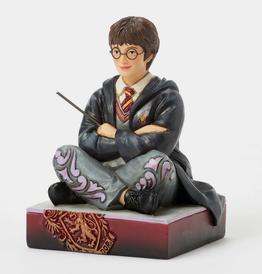 Side of figurine of Harry Potter in a robe, sitting on a box with Gryffindor emblem.
