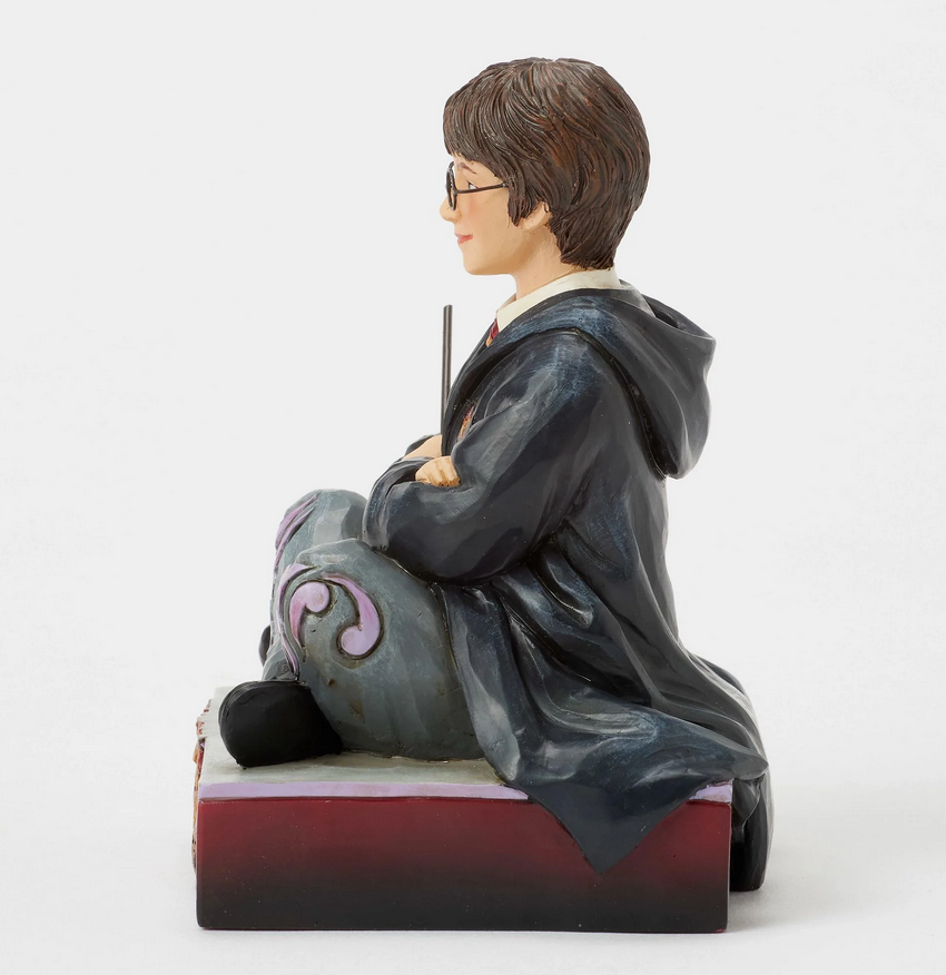 Life side of figurine of Harry Potter in a robe, sitting on a box with Gryffindor emblem.