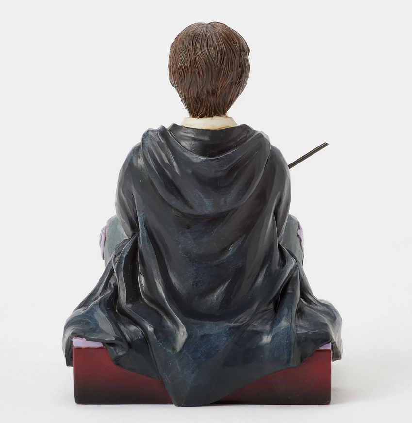 Back of figurine of Harry Potter in a robe, sitting on a box with Gryffindor emblem.