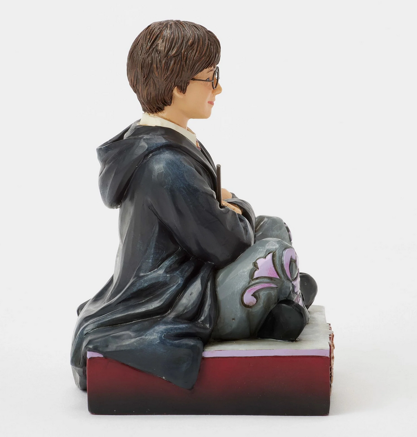 Right side of figurine of Harry Potter in a robe, sitting on a box with Gryffindor emblem.