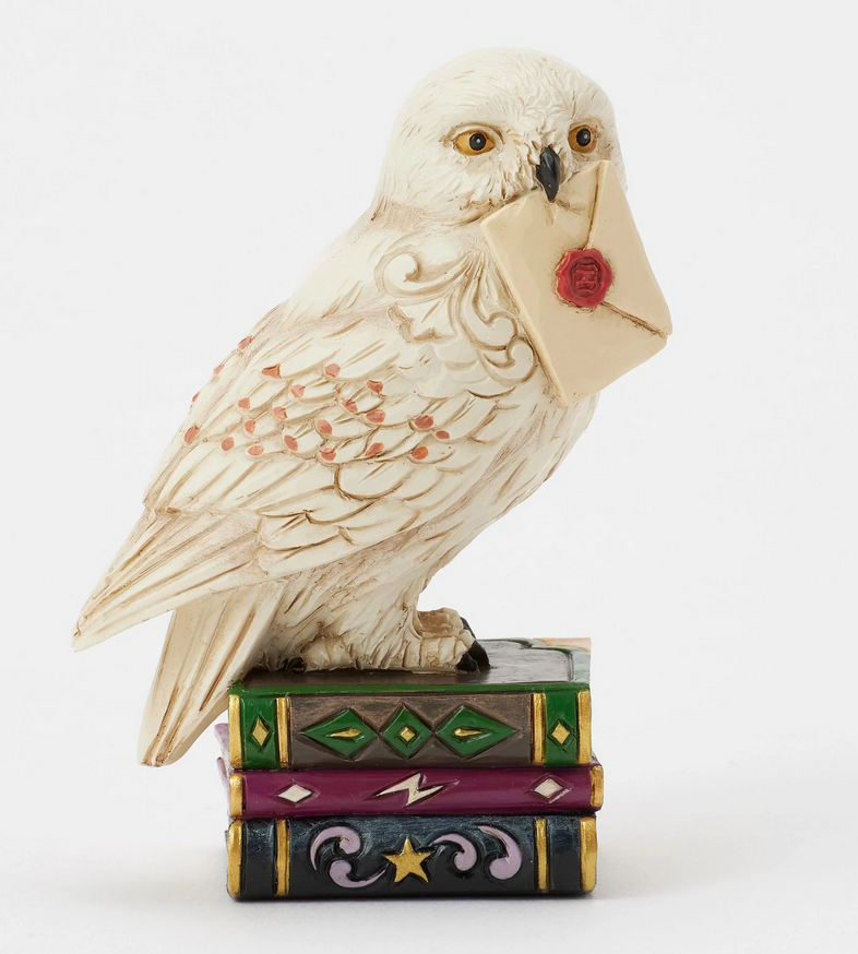 Front of figurine of the owl, Hedwig, with a letter on top of books against a white background
