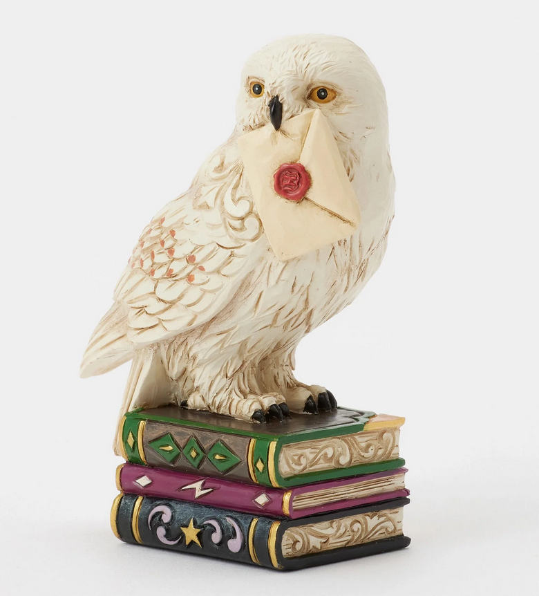 Quarter view of figurine of the owl, Hedwig, with a letter on top of books against a white background