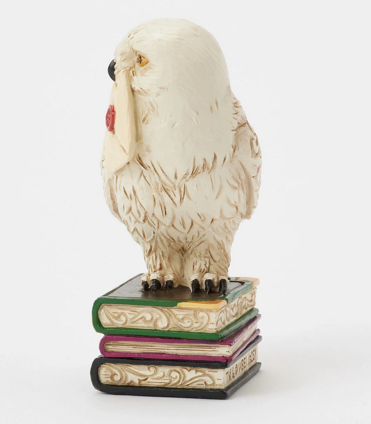 Left side of figurine of the owl, Hedwig, with a letter on top of books against a white background