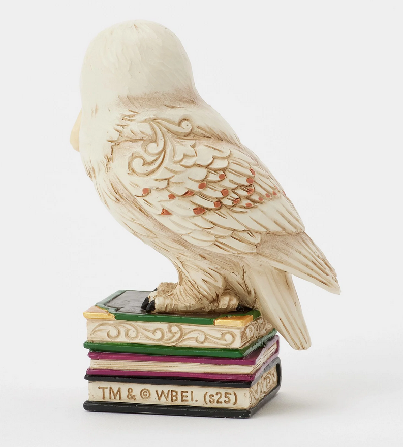 Back of figurine of the owl, Hedwig, with a letter on top of books against a white background
