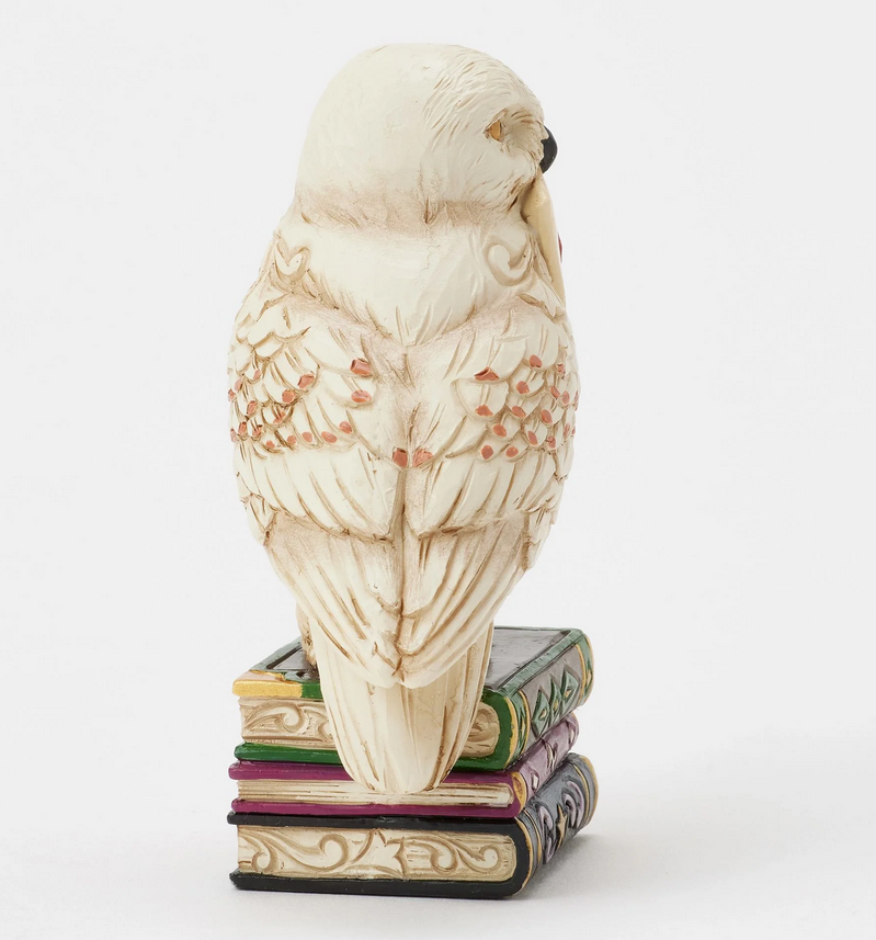 Right side of figurine of the owl, Hedwig, with a letter on top of books against a white background