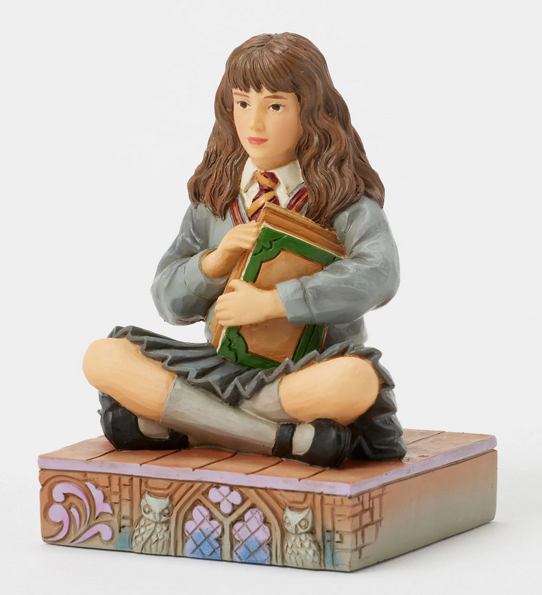 Quarter view of figurine of a Hermine Granger in a school uniform holding books on a decorative base with owl designs.