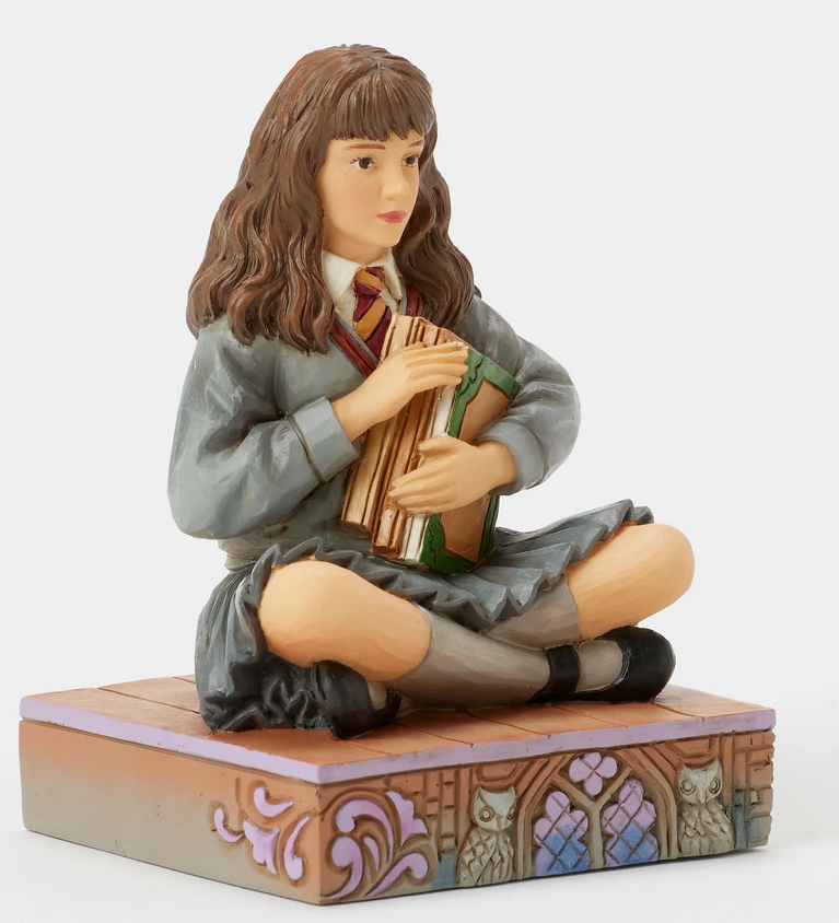 Quarter view of figurine of a Hermine Granger in a school uniform holding books on a decorative base with owl designs.
