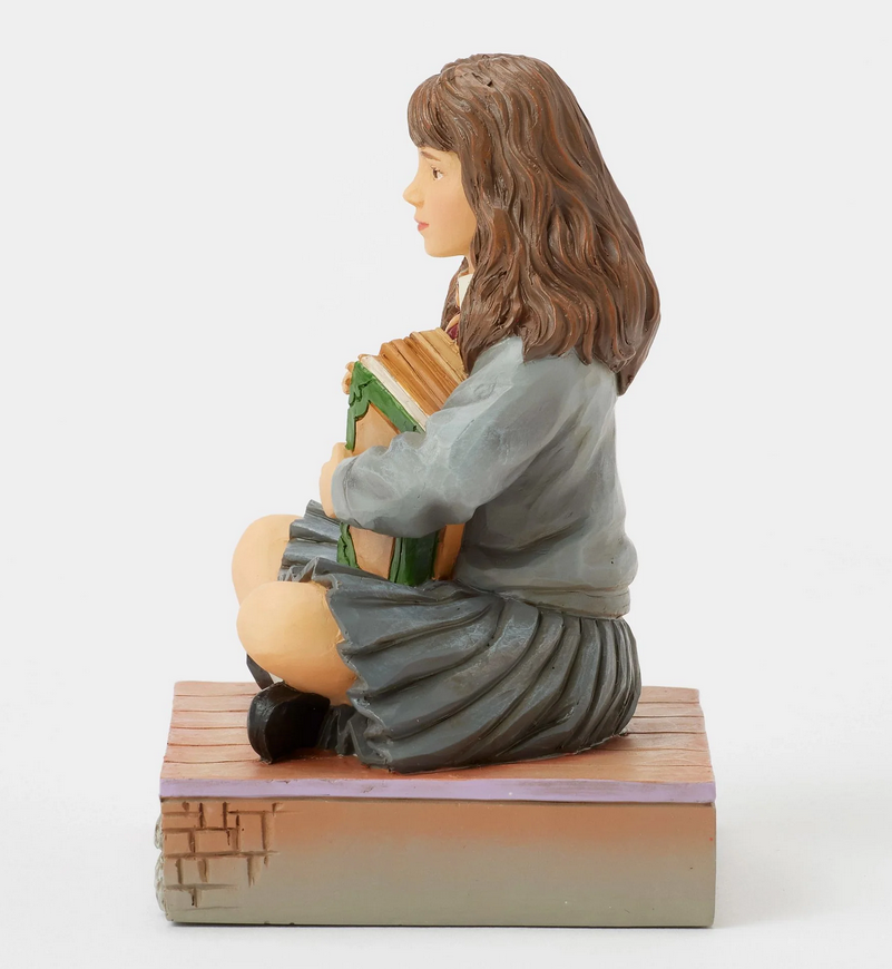 Left side of figurine of a Hermine Granger in a school uniform holding books on a decorative base with owl designs.