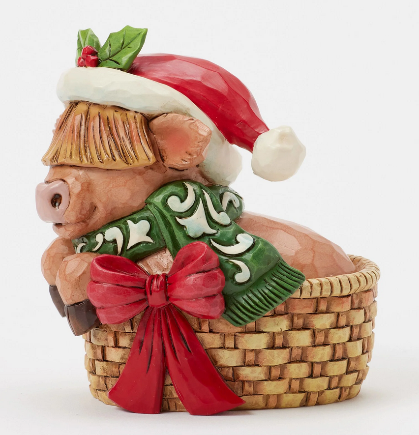 Side of decorative highland cow figurine with a Santa hat, green scarf, in a basket on a white background