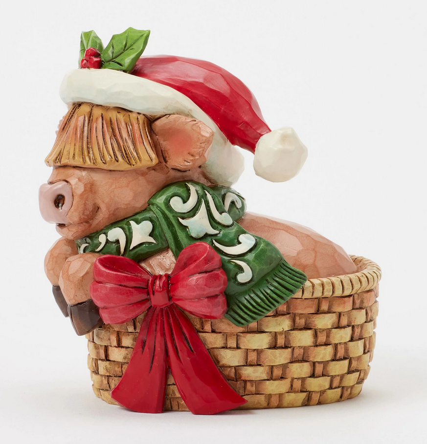 Side of decorative highland cow figurine with a Santa hat, green scarf, in a basket on a white background