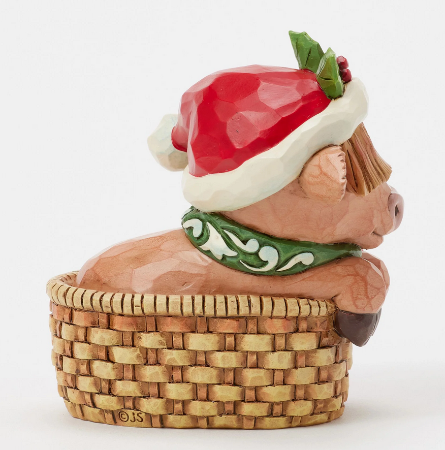 Side of decorative highland cow figurine with a Santa hat, green scarf, in a basket on a white background