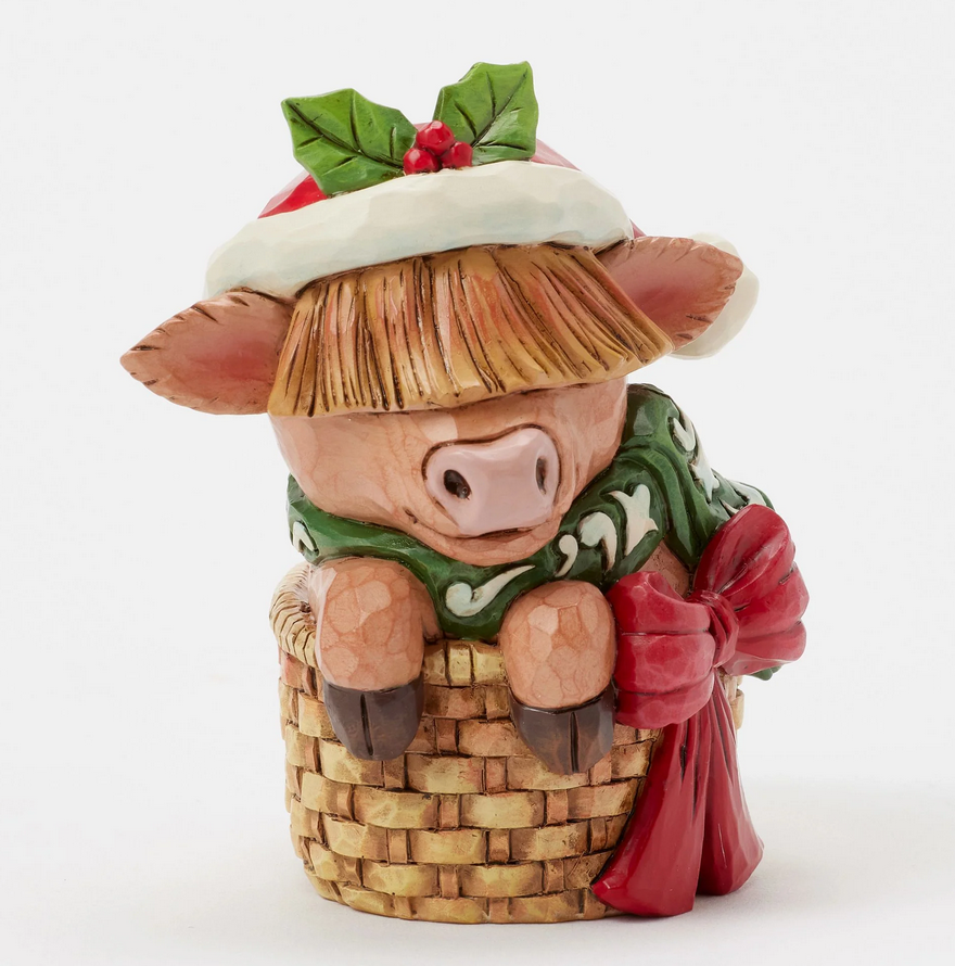 Front of decorative highland cow figurine with a Santa hat, green scarf, in a basket on a white background