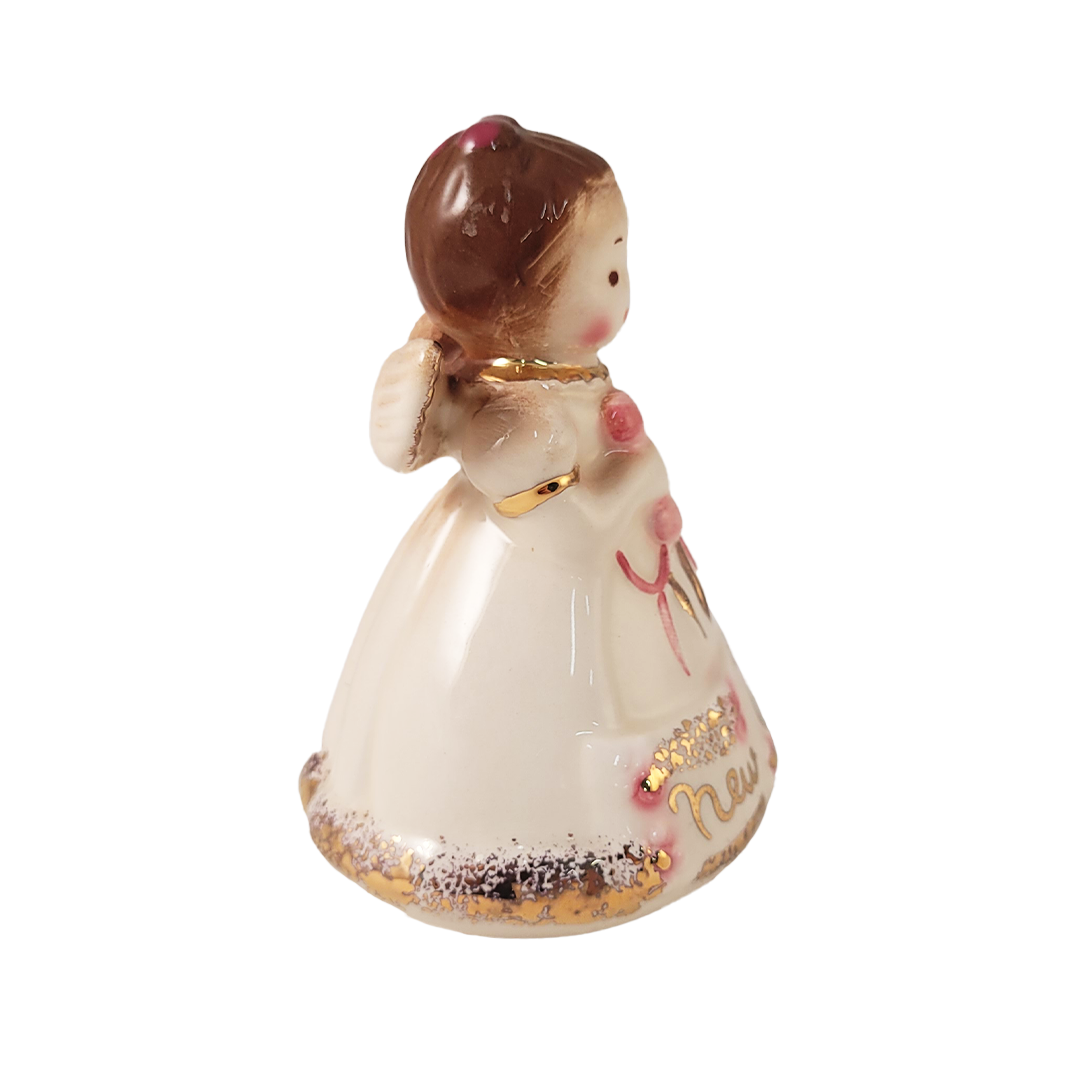 Side of small ceramic angel figurine holding a baby rattle on a white background