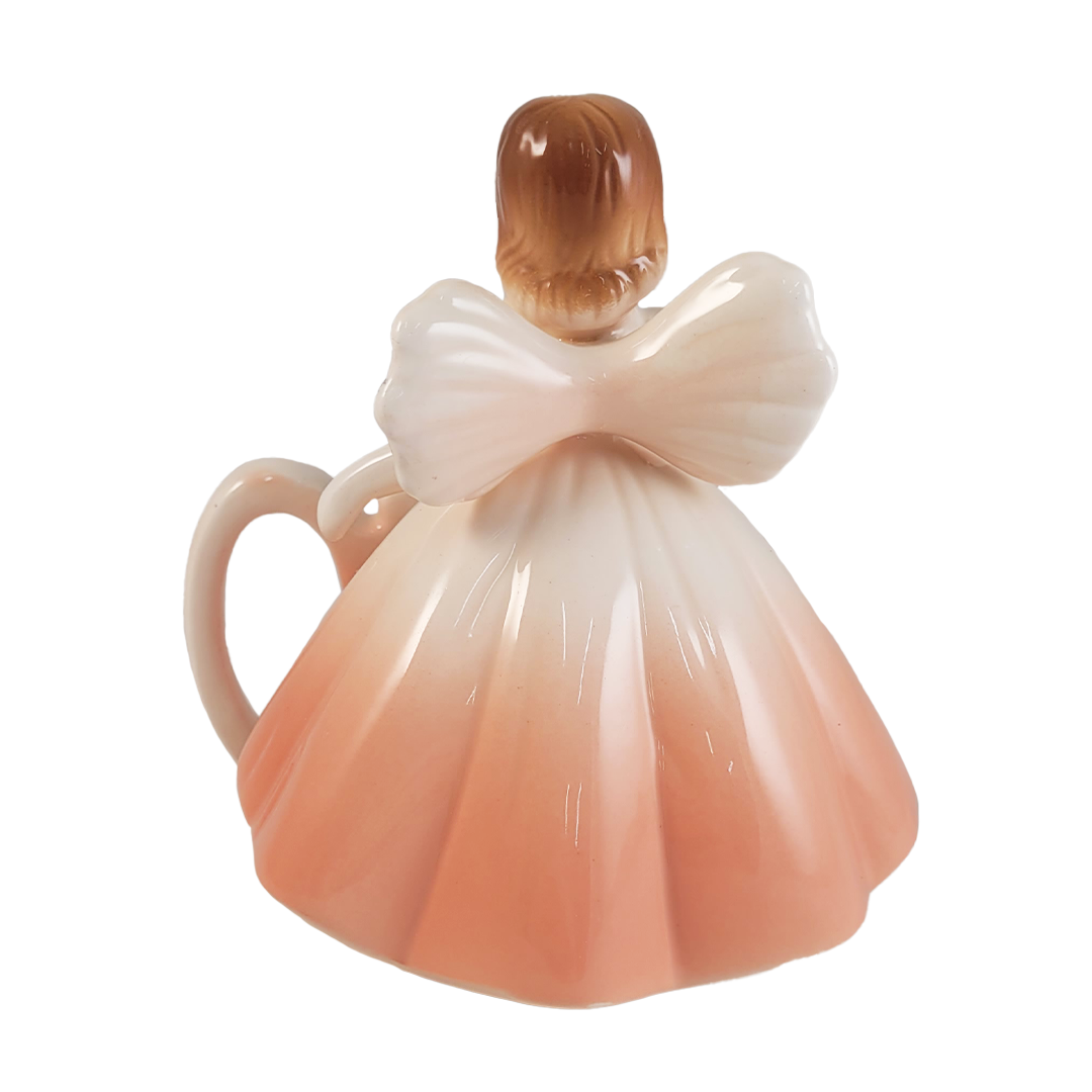 back of angel figurine wearing a peach dress on a white background