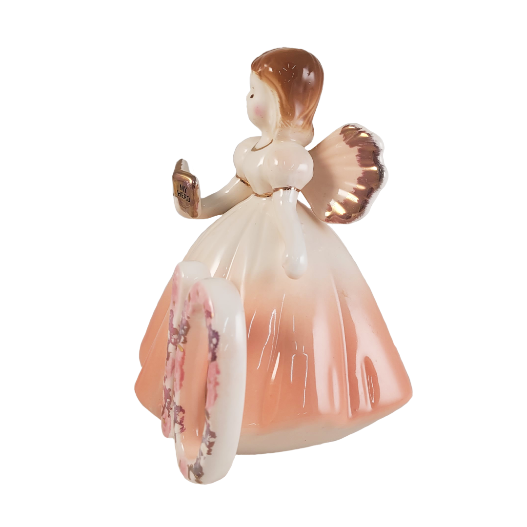 side of angel figurine holding a book and wearing a peach dress on a white background