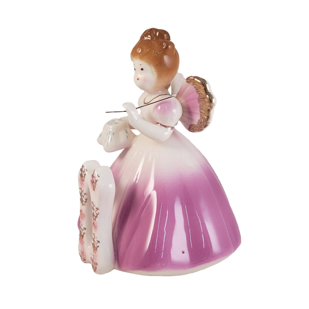 side of angel figurine wearing a purple dress and holding a needle on a white background