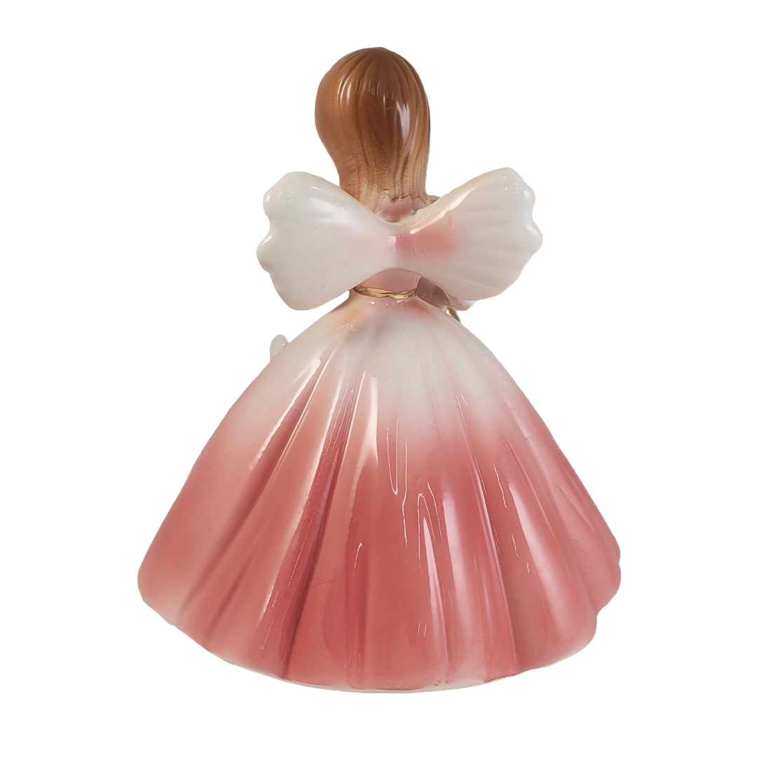Back of angel figurine with a pink dress on a white background