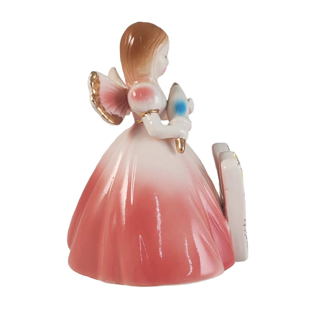 Side of angel figurine holding a parasol wearing a pink dress on a white background