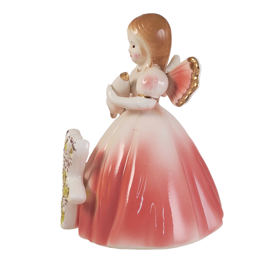 Side of angel figurine holding a parasol wearing a pink dress on a white background