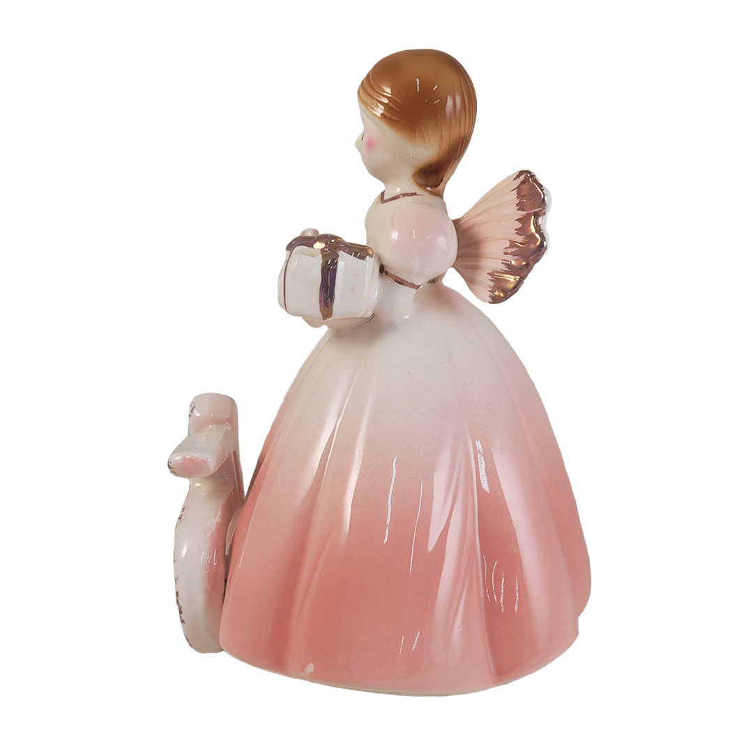 Side of angel figurine holding a gift and wearing a light pink dress on a white background