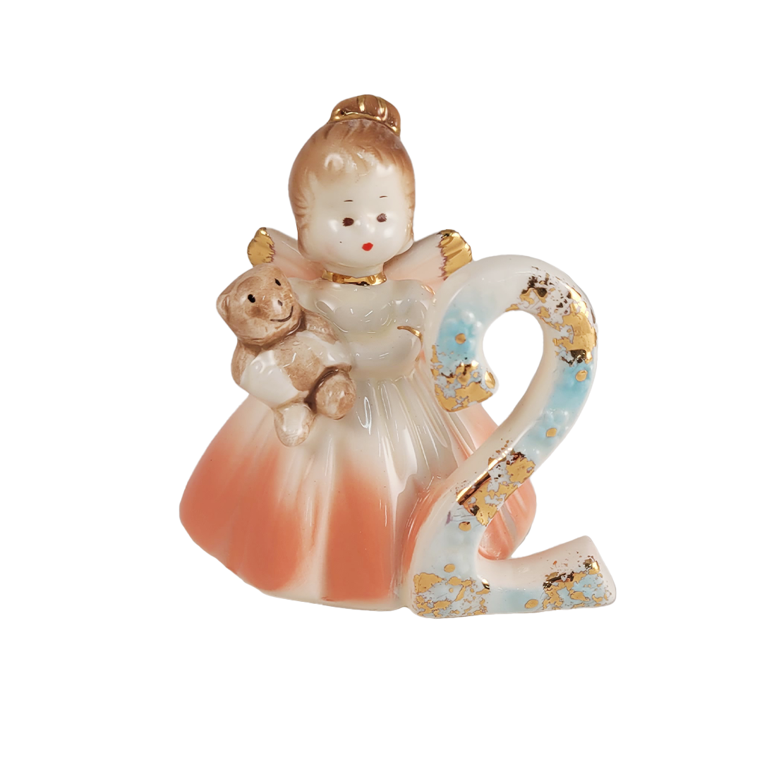 Front of girl angel figurine in peach dress holding a teddy bear with number 2 on a white background
