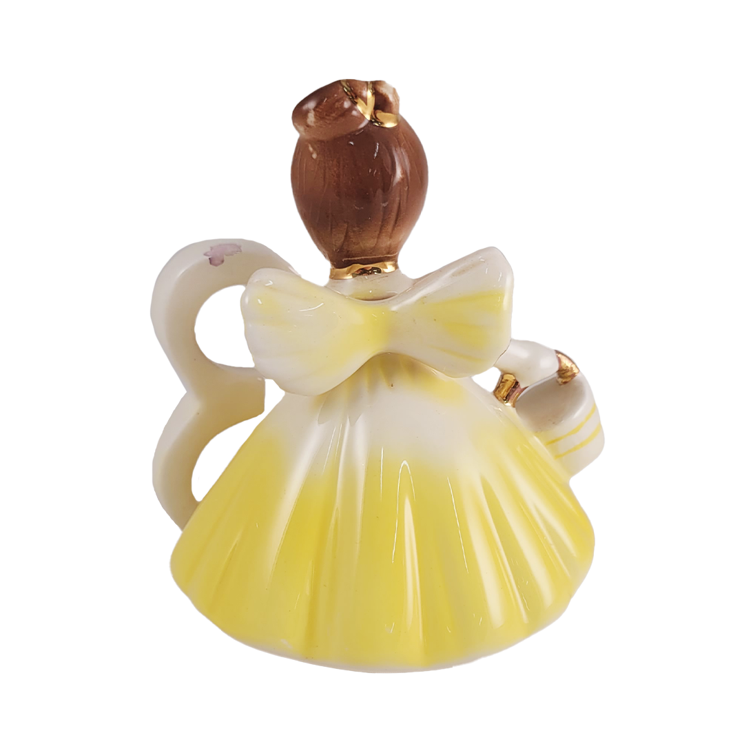Back of ceramic angel figurine with a yellow dress and brown hair on a white background
