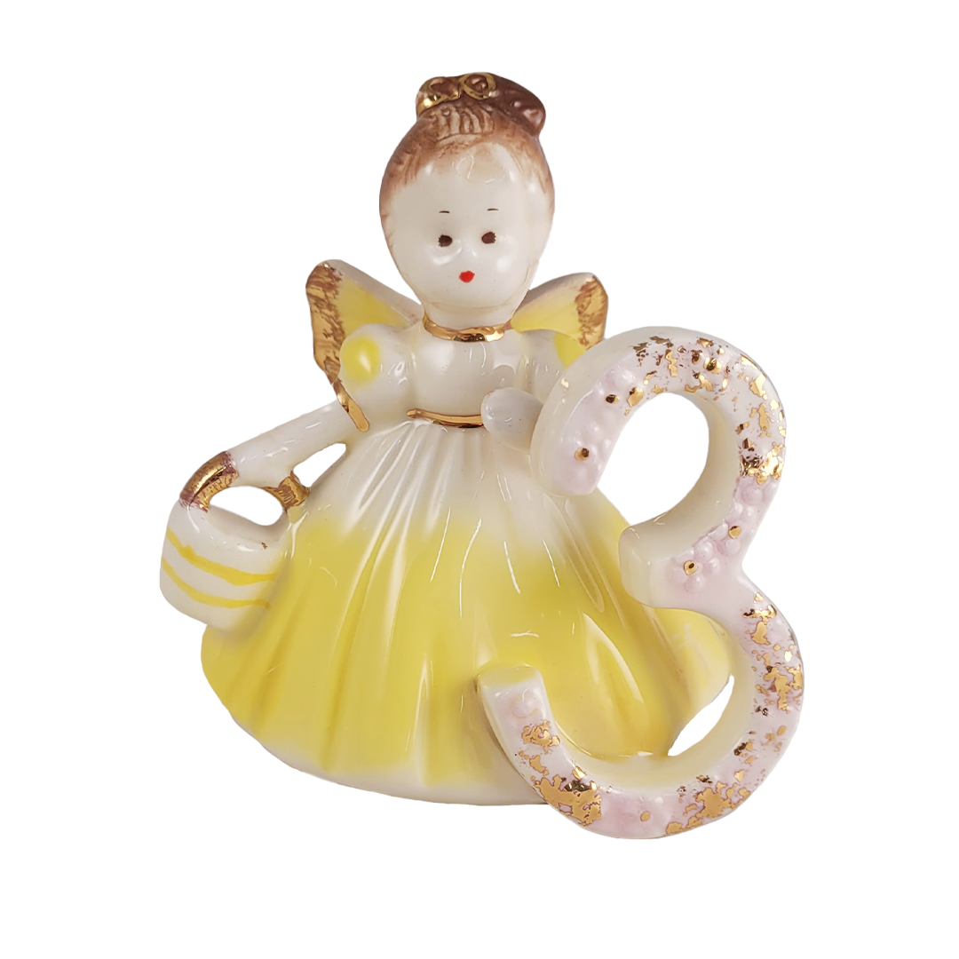 Front of ceramic angel figurine with yellow dress and gold accents on a white background