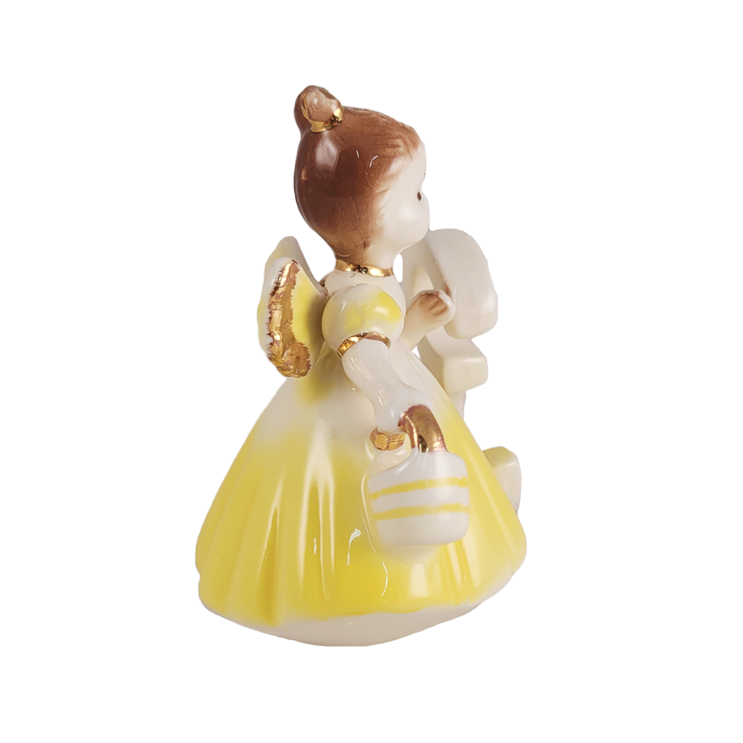 Side of ceramic figurine of a girl in a yellow dress with a white background