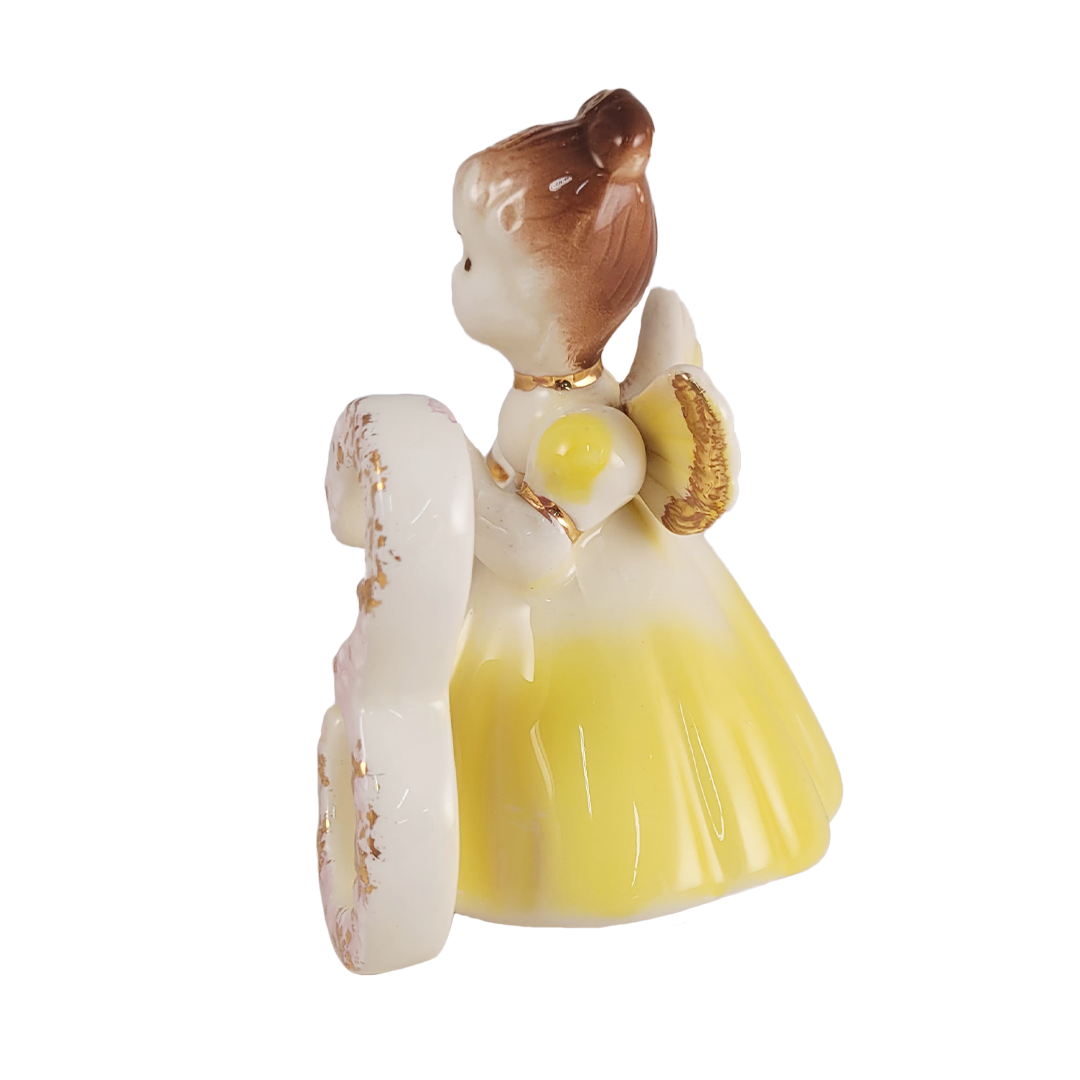 Side of ceramic angel figurine with a yellow dress and brown hair on a white background