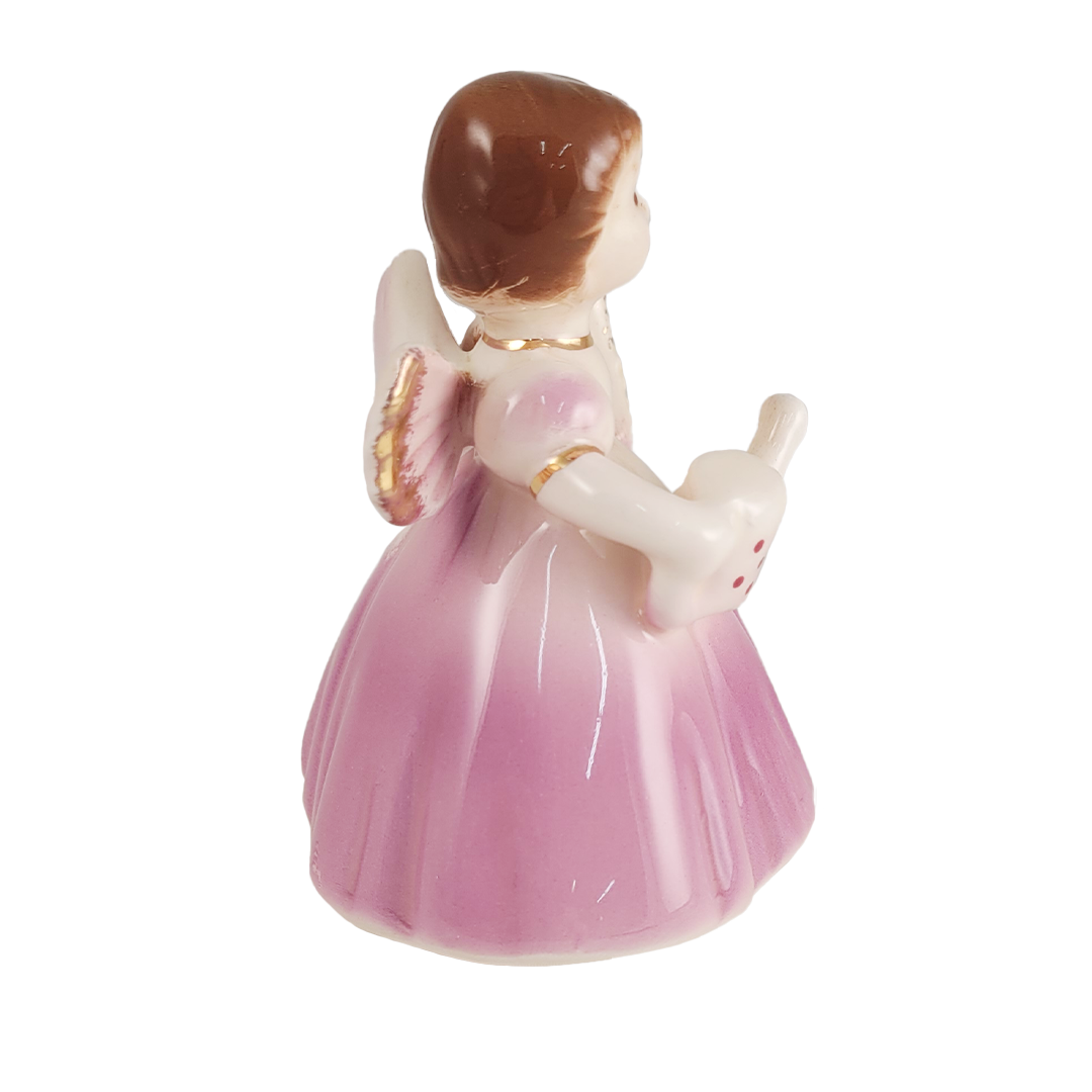 Side of small angel figurine in a pink dress holding a teapot on a white background