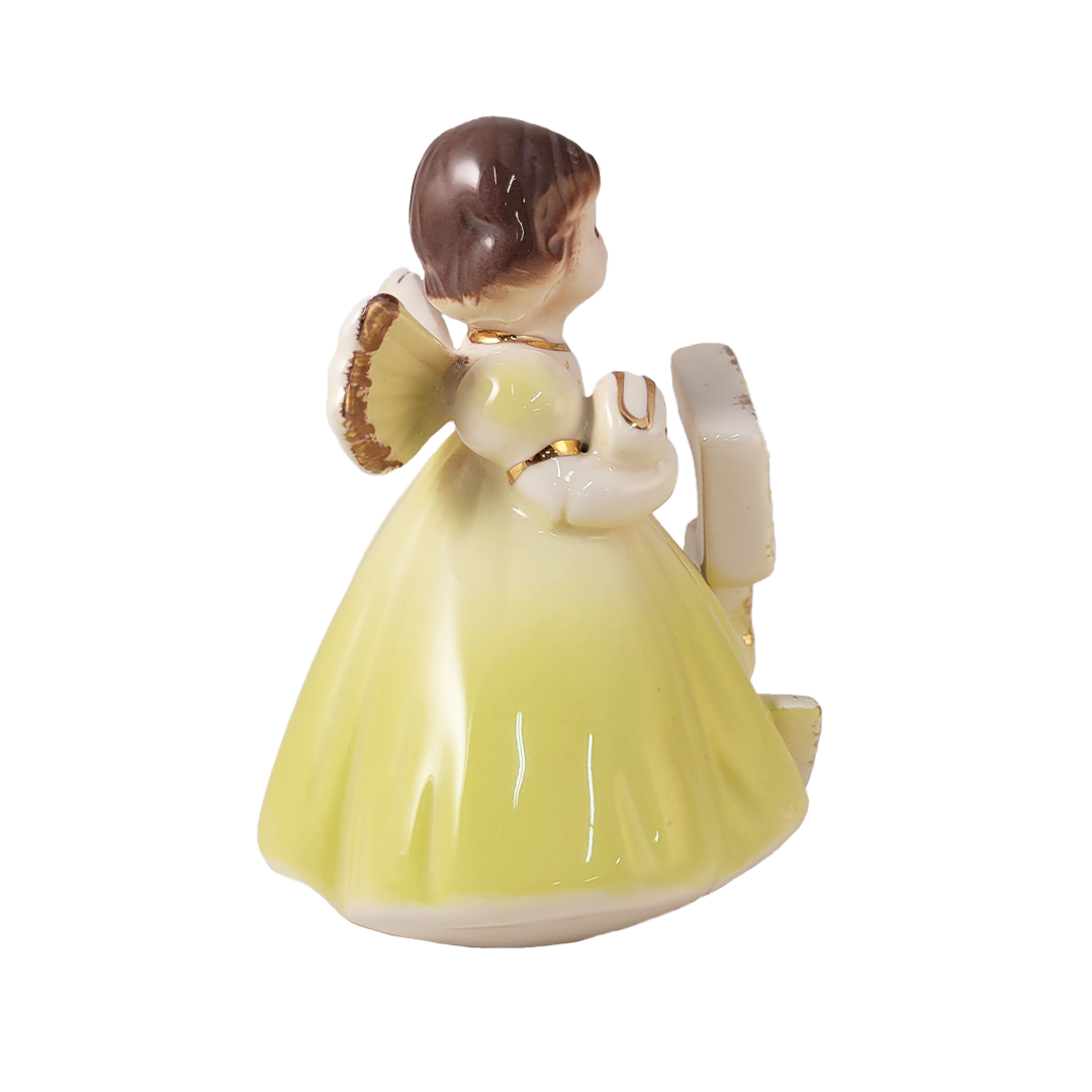 Side of angel figurine with a yellow dress on a white background