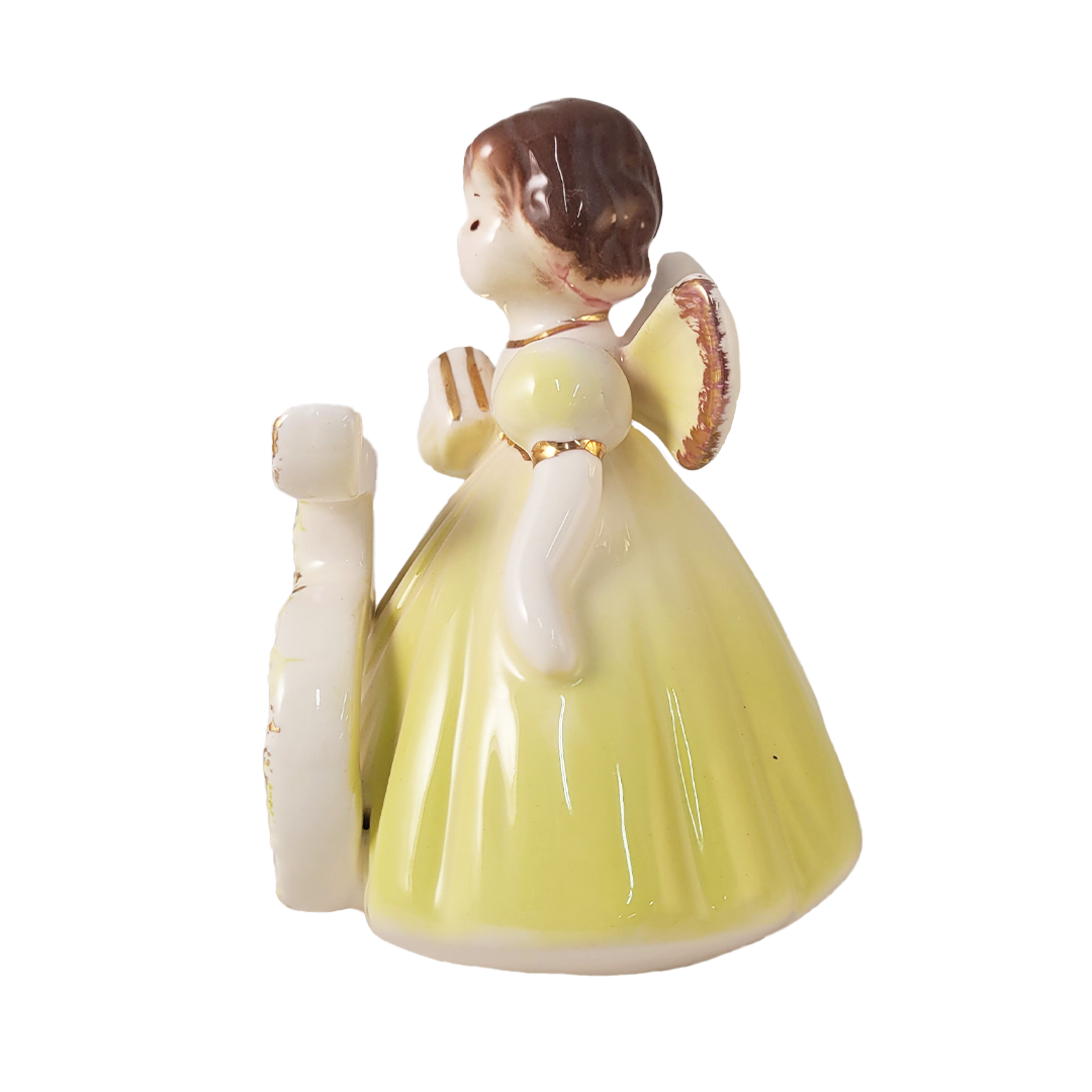 Porcelain figurine of a girl in a yellow dress holding a book on a white background