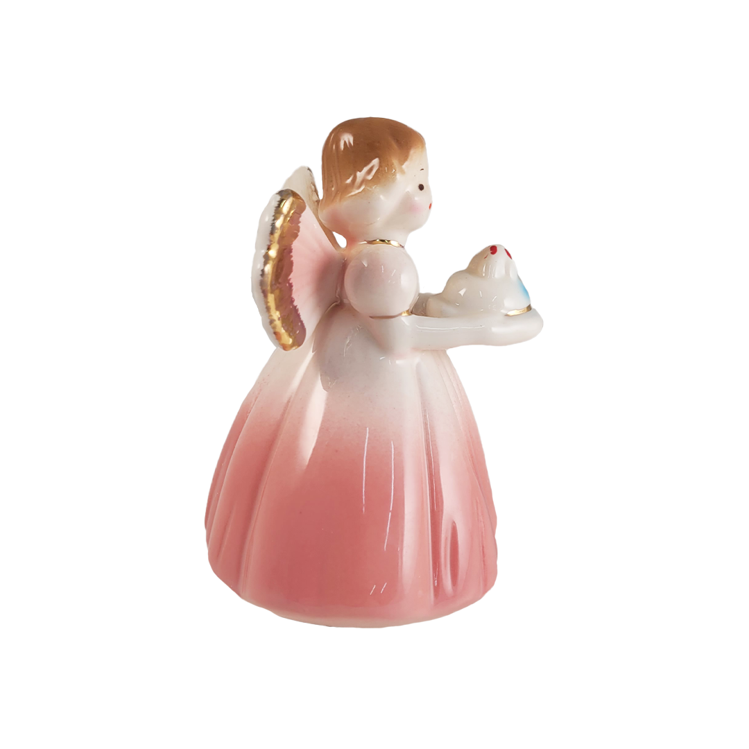 Side of porcelain angel figurine with a pink dress and gold wings holding a cake on a white background