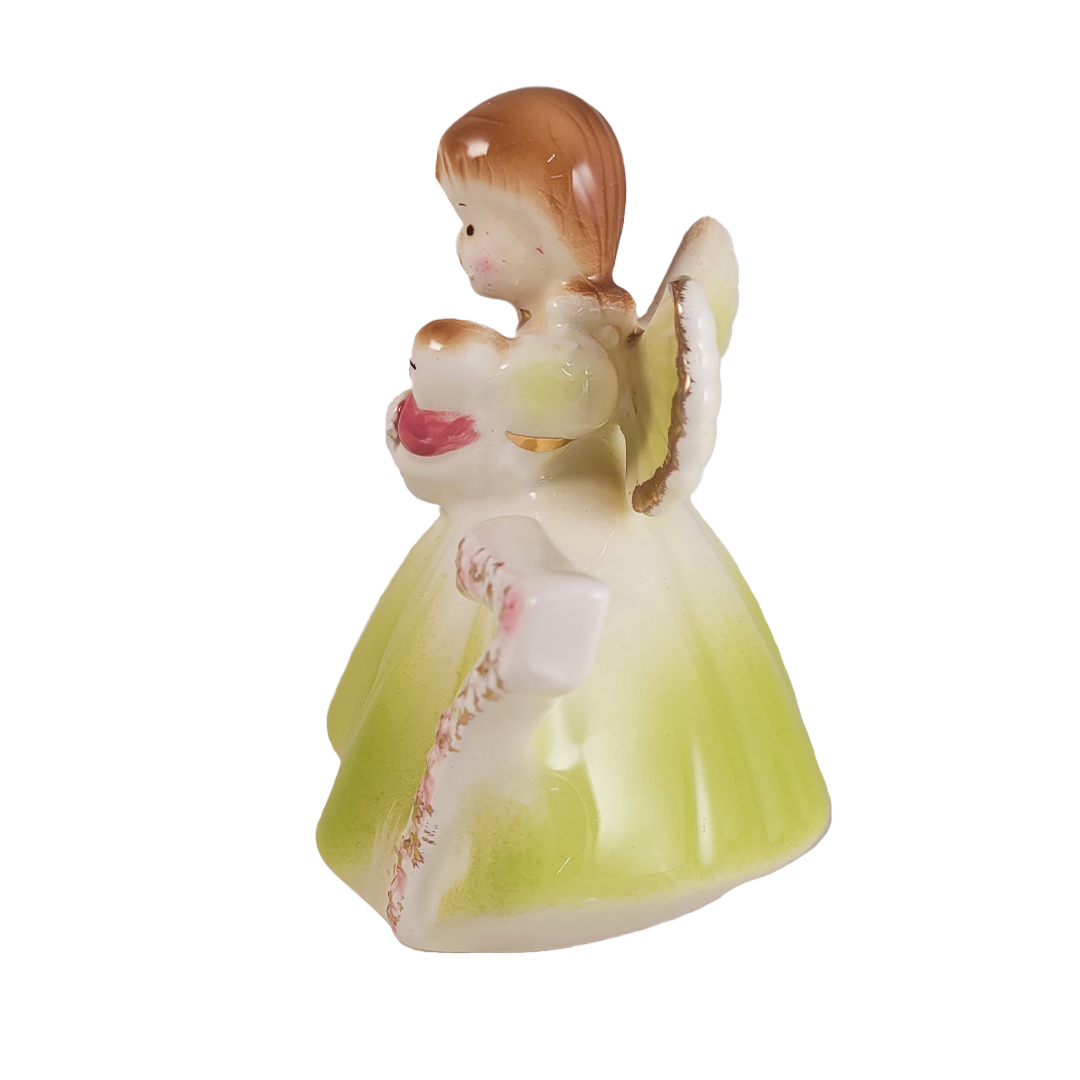 Side of porcelain angel figurine with a green dress and brown hair on a white background