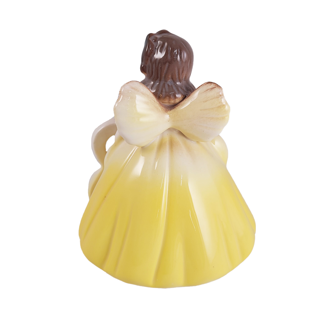 Back of angel figurine in a yellow dress with a brown head on a white background