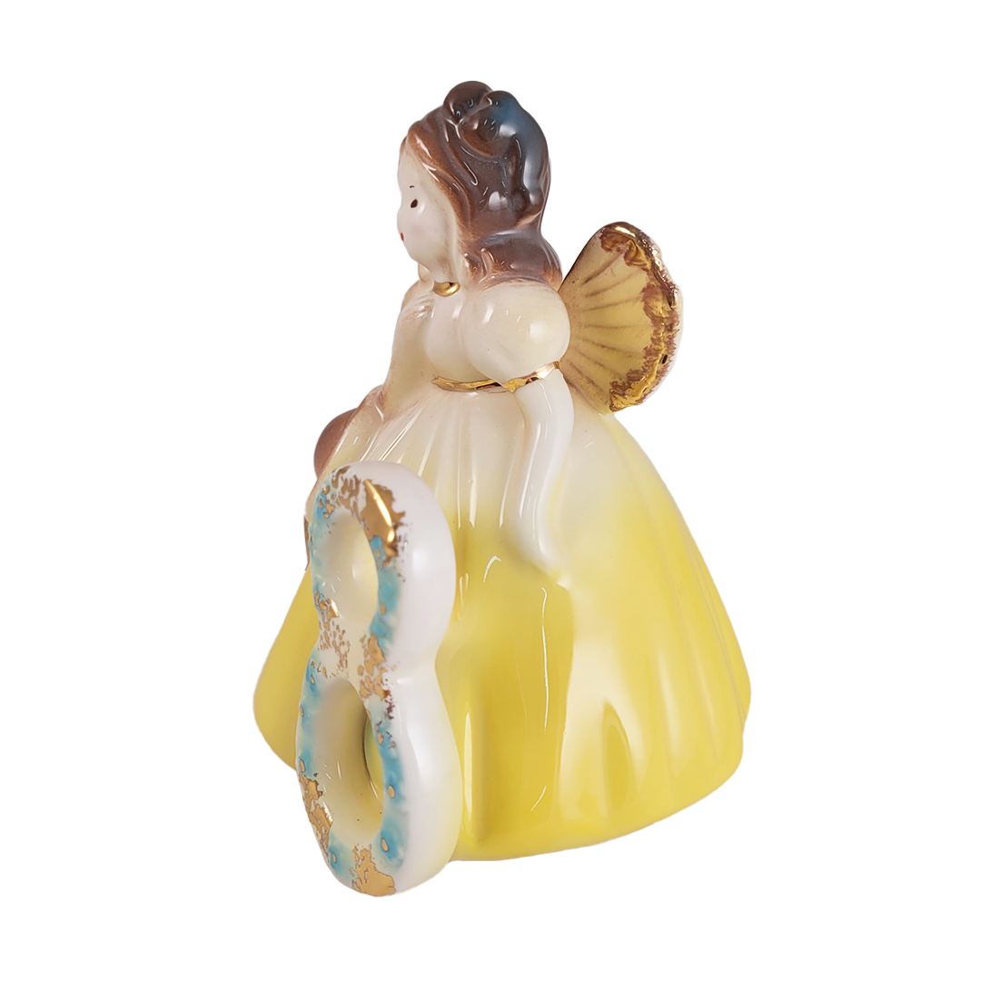 Side of angel figurine with yellow dress and brown hair on a white background